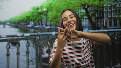 Fototapeta premium Woman making hashtag hand sign with fingers on a canal street bridge in amsterdam; social sharing joy.