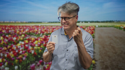 Man holding creditcard in hand smiling broadly while pointing finger to card on a rural flower field path street; happiness convenience.
