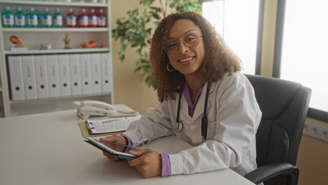 Transgender hispanic woman doctor wearing stethoscope holding tablet with hands reading patient records in clinic; dedication. - Powered by Adobe