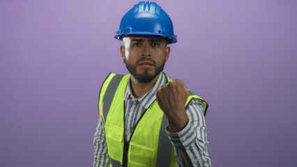 Man engineer with blue hardhat and high visibility vest showing clenched fist in purple studio; determination safety.