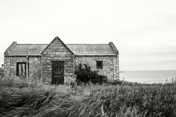 Old abandoned house made of stone by the sea against the background of sky and grass. Color of the Year 2026, Cloud Dancer.