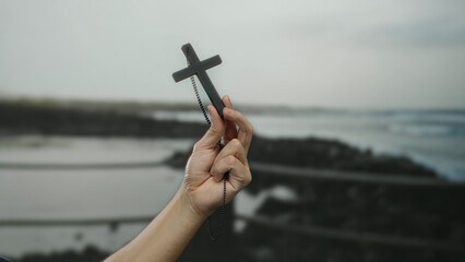 Man holding cross at seaside beach, showcasing faith, spirituality, oceanic background, and religious symbolism.