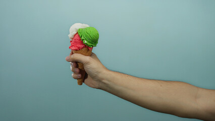Man holding colorful ice cream cone against blue background, showcasing vibrant colors and...