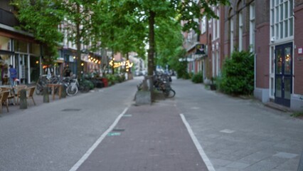 Fototapeta premium Defocused view of a charming european street lined with bicycles, cafes, and lush trees, creating a serene urban ambiance in an outdoor european city setting.