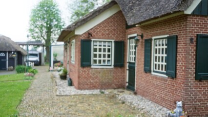 Blurred image of a charming house with brick walls and green shutters surrounded by lush greenery, conveying a peaceful rural lifestyle.