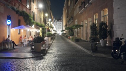 Blurred cobblestone street at night with soft bokeh lights and sidewalk cafe outdoor; background backplate copyspace calm.