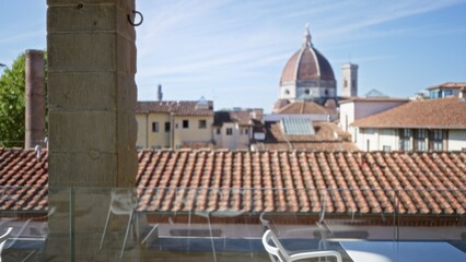 Fototapeta premium Rooftop terrace view with terracotta tile roofs and distant cathedral dome, soft defocused bokeh in a sunny city; background copyspace overlay.