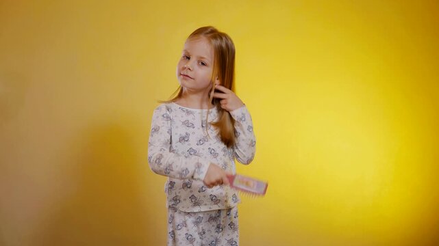 Young girl in patterned pajamas combs her hair with a comb. The child does her hair in the morning after sleep.