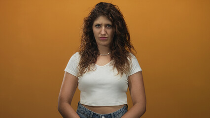 Young hispanic woman with visible midriff standing facing camera in orange studio wearing white...