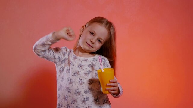 Young girl in patterned pajamas mid-yawn with arms stretched wide against a vibrant orange backdrop. Wide-open mouth of a sleepy child stretching in light-colored, printed sleepwear.