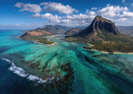 Aerial view showcases a turquoise ocean with a dramatic mountain backdrop under a partly cloudy sky