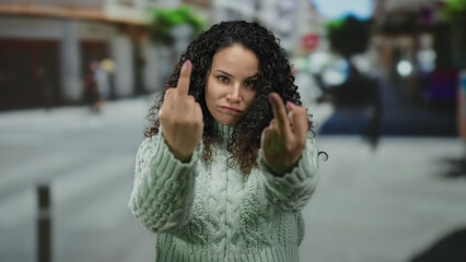Woman outdoors with curly hair wearing sweater showing anger with hand gesture on urban street background, expressing frustration in city setting.