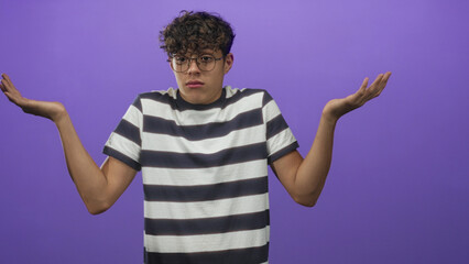 Boy shrugging with palms up, hands visible, wearing black and white striped shirt in a purple studio setting; uncertainty questioning.