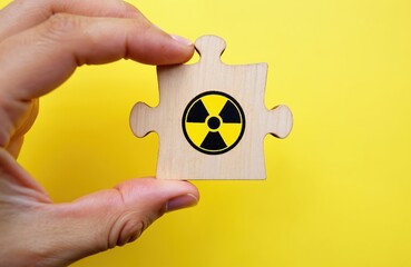 Hand holds wooden puzzle piece with radiation symbol. Danger alert symbol signifies radioactive hazard warning. Safety precaution concept for hazardous materials.