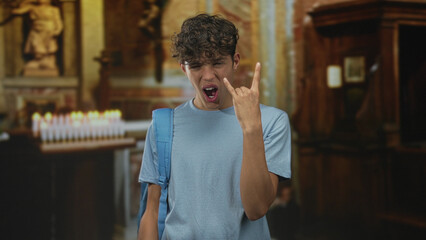 Teenage boy wearing blue backpack flashes rock hand gesture and sticks tongue visible in front of...