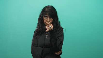 Woman senior hispanic points finger to eye in studio wearing black top and silver pendant while...