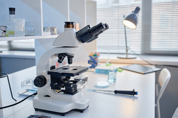 Laboratory microscope standing on workbench surrounded by scientific glassware and pipette, laboratory equipment arranged for research or analysis in modern science facility