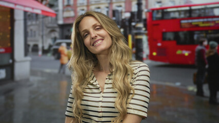 Confident woman hair flowing while smiling on a busy street with young blonde outdoors vibe in an urban city landscape as a red bus passes by.