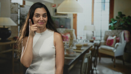 Young hispanic woman points finger to head in a living room building, smiling and expressive; idea inspiration thoughtful.