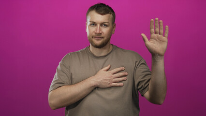 Young caucasian man placing hand on chest and raising the other palm in a magenta studio; honor commitment integrity.