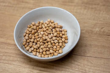 Dry chickpeas in a ceramic bowl on a wooden table. Healthy ingredient used for salads, soups, hummus, and plant-based meals. High in protein and fiber.