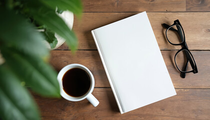 Flat lay top view of white blank book mockup beside eyeglasses and coffee cup on brown wooden table. Green plant leaves in foreground. Customizable template for literature, reading, or design.