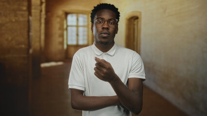 Young african american man pointing finger to head in old building illuminated by window light; pensive introspection.