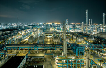 Night view of the illuminated petrochemical industrial zone with pipelines and storage tanks.