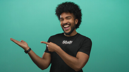 Smiling man in staff uniform points confidently at hand against vibrant green background, engaging...