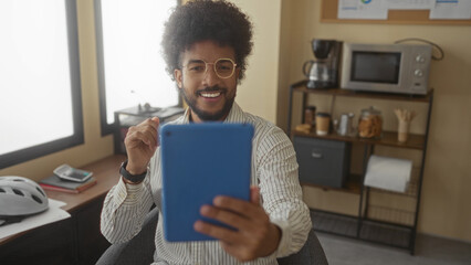 Man using tablet in office with modern interior and appliances, seated by window, appearing engaged and focused in indoor workplace.