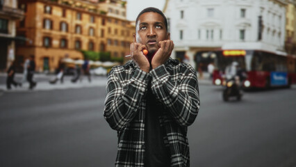 Man holding orange screwdriver to mouth with hands on street beside a red city bus, wearing...