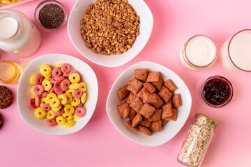 Dry breakfast and milk. Dry sweet breakfast - corn rings, chocolate corn pillows and granola, milk, yogurt and honey on a pink background. Quick and nutritious breakfast