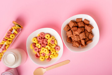 Dry breakfast and milk. Dry sweet breakfast - corn rings, chocolate corn pillows, milk, yogurt and honey on a pink background. Quick and nutritious breakfast