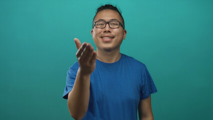 Man extending hand for handshake, wearing blue t shirt in teal studio with outstretched palm...