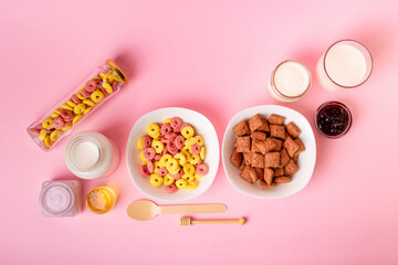 Dry breakfast and milk. Dry sweet breakfast - corn rings, chocolate corn pillows, milk, yogurt and honey on a pink background. Quick and nutritious breakfast