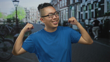 Man smiling holding fists to chest wearing glasses and blue t shirt on street; confidence community.