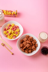 Dry breakfast and milk. Dry sweet breakfast - corn rings, chocolate corn pillows, milk, yogurt and honey on a pink background. Quick and nutritious breakfast
