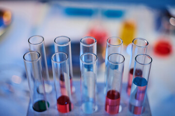 Closeup showing empty and partially filled glass test tubes in laboratory rack, various colored liquids visible inside tubes, scientific research or chemical experiment setting
