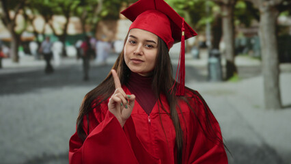 Young woman in graduation cap and gown poses outdoors on a street, celebrating education...