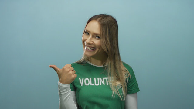 Smiling woman wearing green volunteer shirt giving thumbs up on blue isolated background