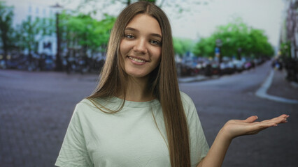 Girl on a city street smiling while holding her hand palm up gesture presenting the scene;...