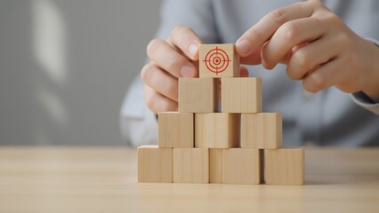 Achieving strategic success A hand places a target block on a rising pyramid of wooden cubes, illustrating focused goal setting, business development, and a clear path to future growth