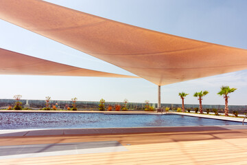 modern outdoor pool with sun shade sails and palm trees on a sunny resort deck