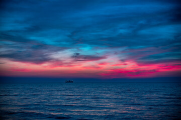 Obraz premium Silhouette of Cargo Ship on Calm Ocean at Dusk Under Colorful Sunset Sky Over Horizon