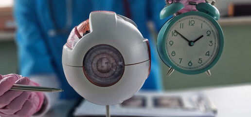 Ophthalmologist shows time on alarm clock holding eye model