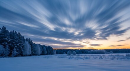 Streaky clouds drift across a snowy forest landscape at dusk.