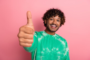 Young smiling man gives thumbs up in green tie dye shirt against pink background for lifestyle fashion advertising