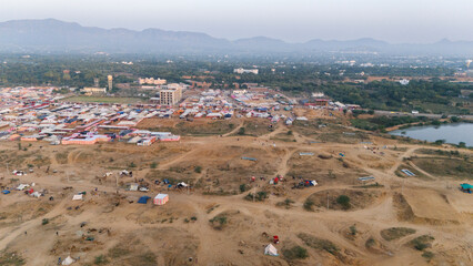 Aerial view of camel and horse tents with a pond in the Pushkar desert area during the Pushkar Cattle Fair on a winter morning, with Aravali mountains in the background, capturing vibrant fairground