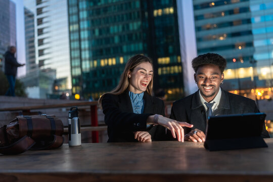 Diverse coworkers collaborating outdoors with tablet at night