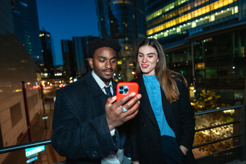 Diverse business people sharing smartphone screen downtown night